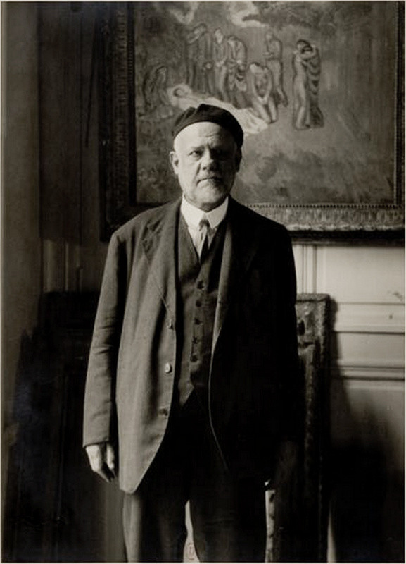 AMBROISE VOLLARD, STANDING IN FRONT OF PICASSO’S EVOCACIÓN EL ENTIERRO DE CASAGEMAS